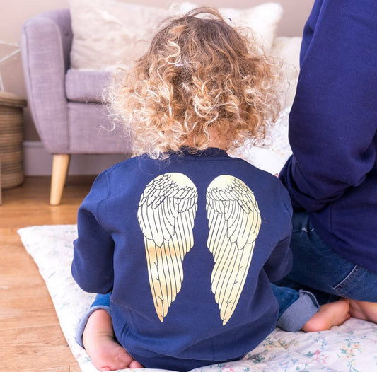 girl wearing navy jumper with gold foil angel wings printed on the back